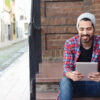 Latino man sitting on steps smiling in front of a work tablet