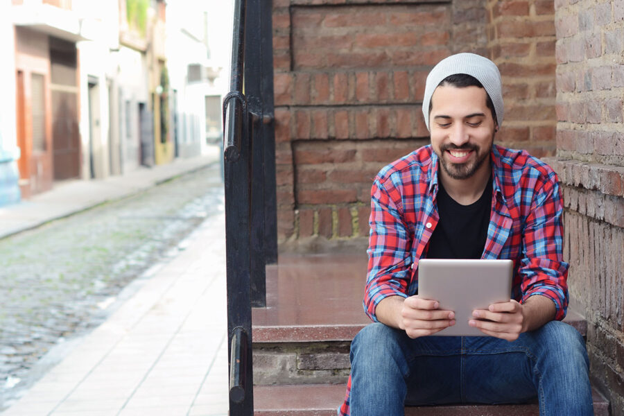 Latino man sitting on steps smiling in front of a work tablet