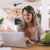 Smiling woman sitting in front of a laptop in a tropical cafe