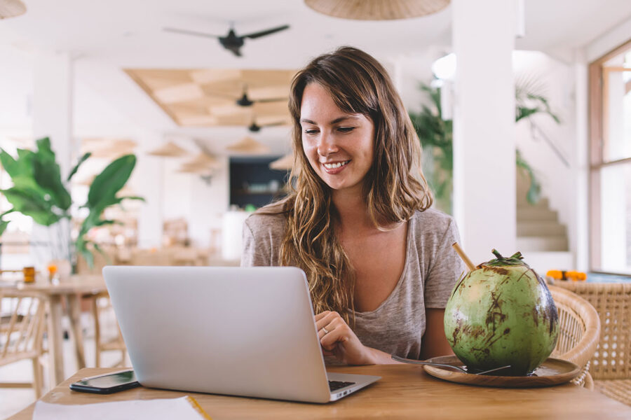 Smiling woman sitting in front of a laptop in a tropical cafe
