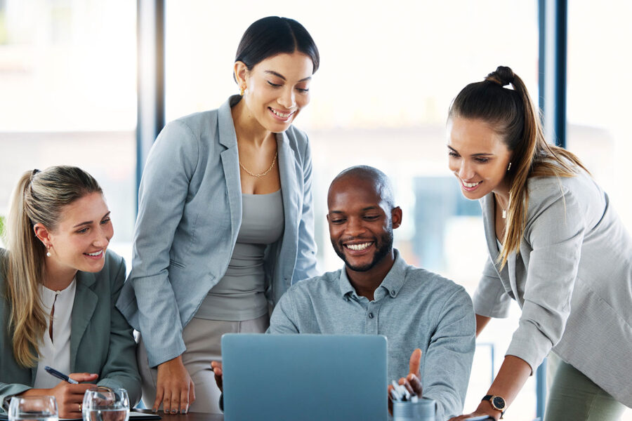 Team of four diverse co-workers smiling looking at a laptop